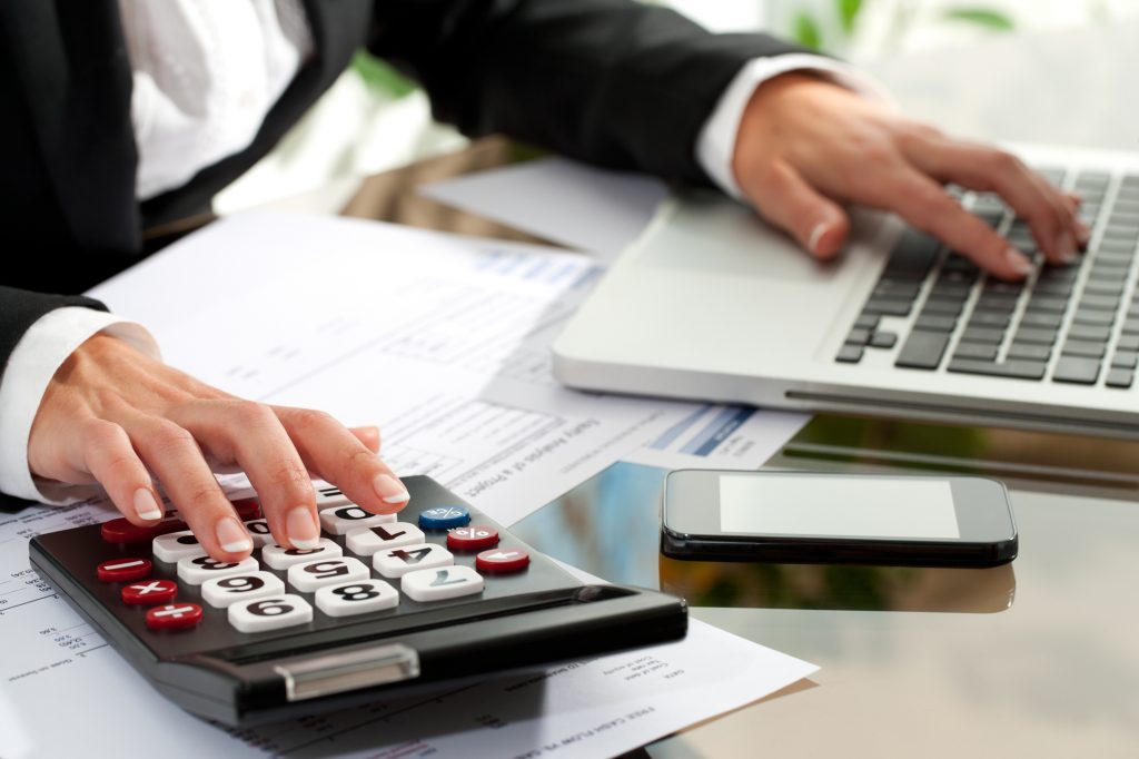 Close up of female hands working on calculator and laptop.